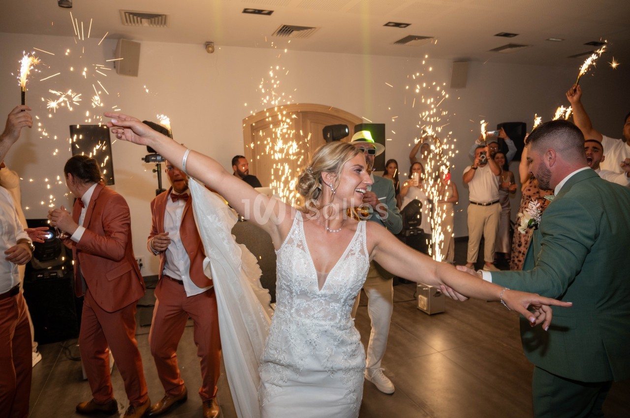 Une mariée danse joyeusement entourée d'invités et de feux d'artifice intérieurs dans une salle de réception.