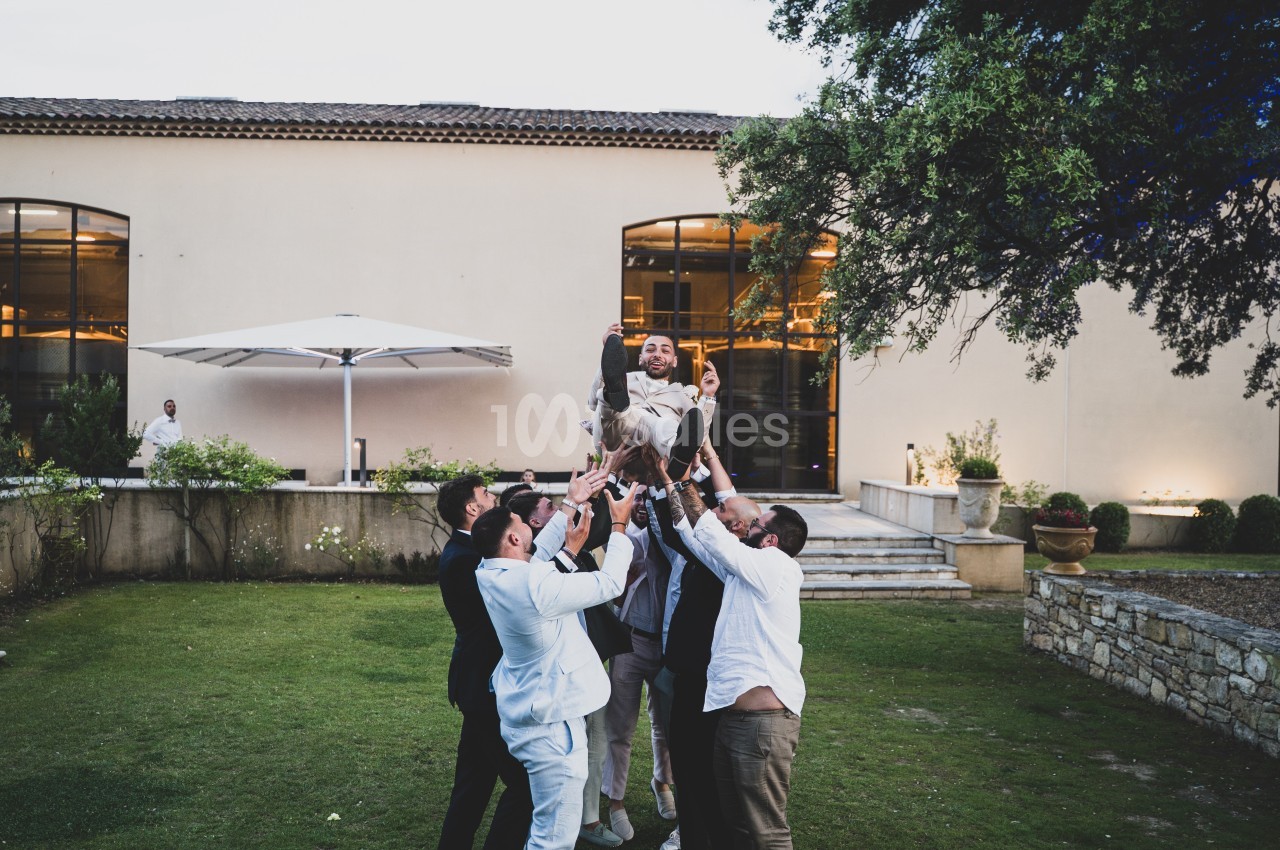 Un groupe d'hommes soulève une personne en l'air dans un jardin devant un bâtiment moderne.