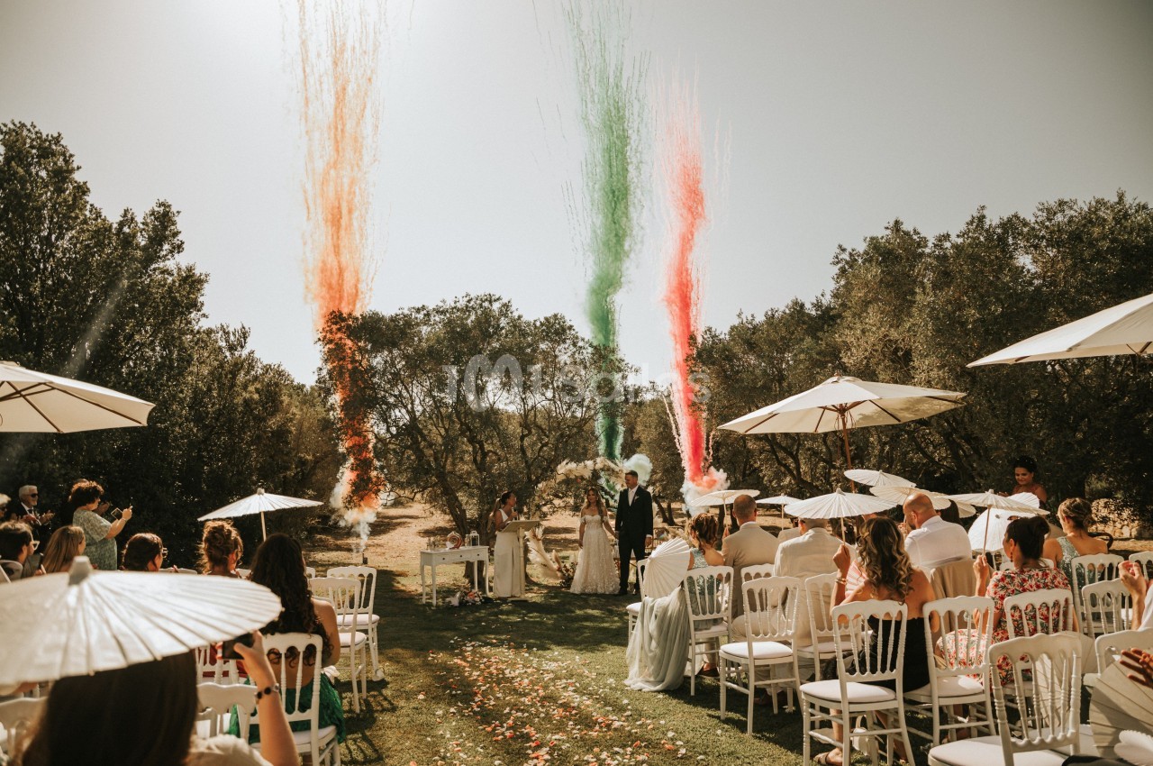 Cérémonie de mariage en extérieur avec des invités assis, des jets de fumée colorée et un couple à l'autel.