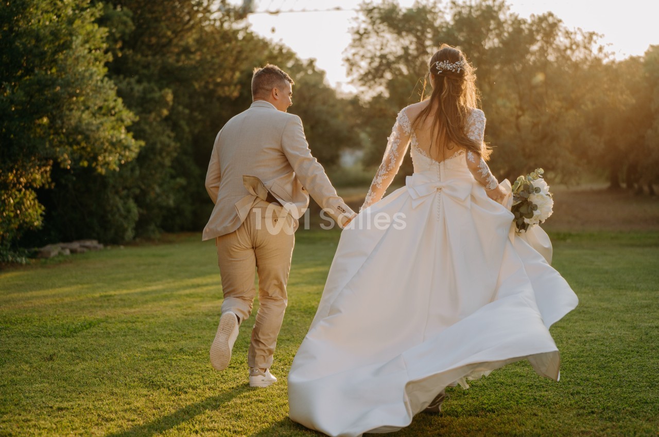 Un couple en tenue de mariage court sur une pelouse verdoyante au coucher du soleil.