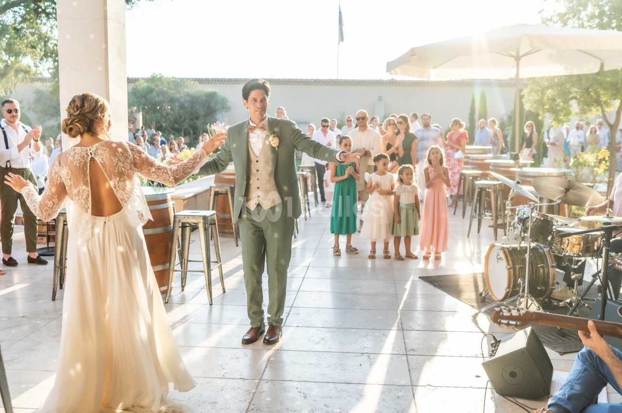 Un couple danse en extérieur lors d'une réception, entouré d'invités et d'enfants sous une lumière ensoleillée.