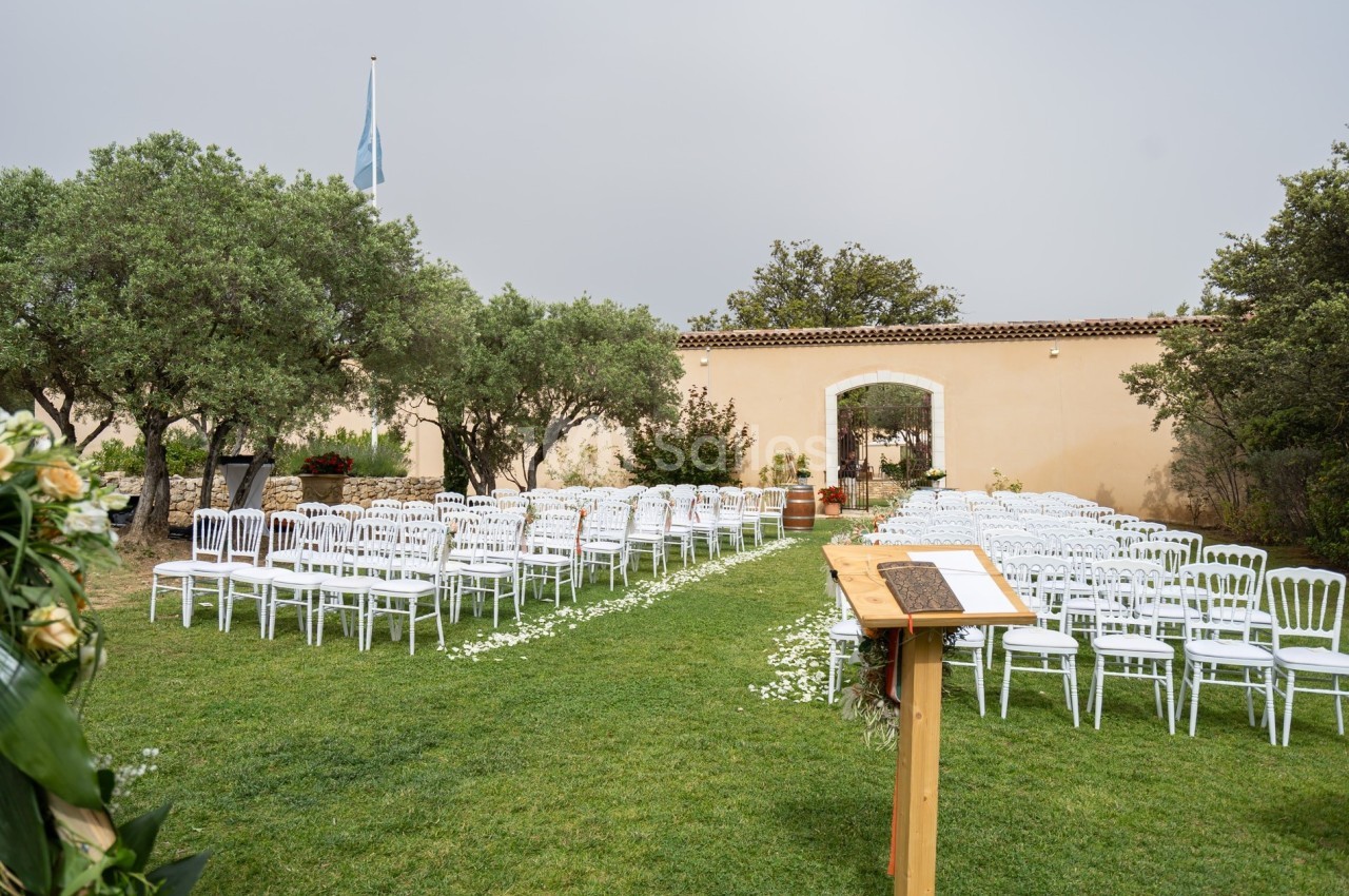 Chaises blanches disposées en rangées sur une pelouse pour une cérémonie en extérieur, avec un pupitre au premier plan.