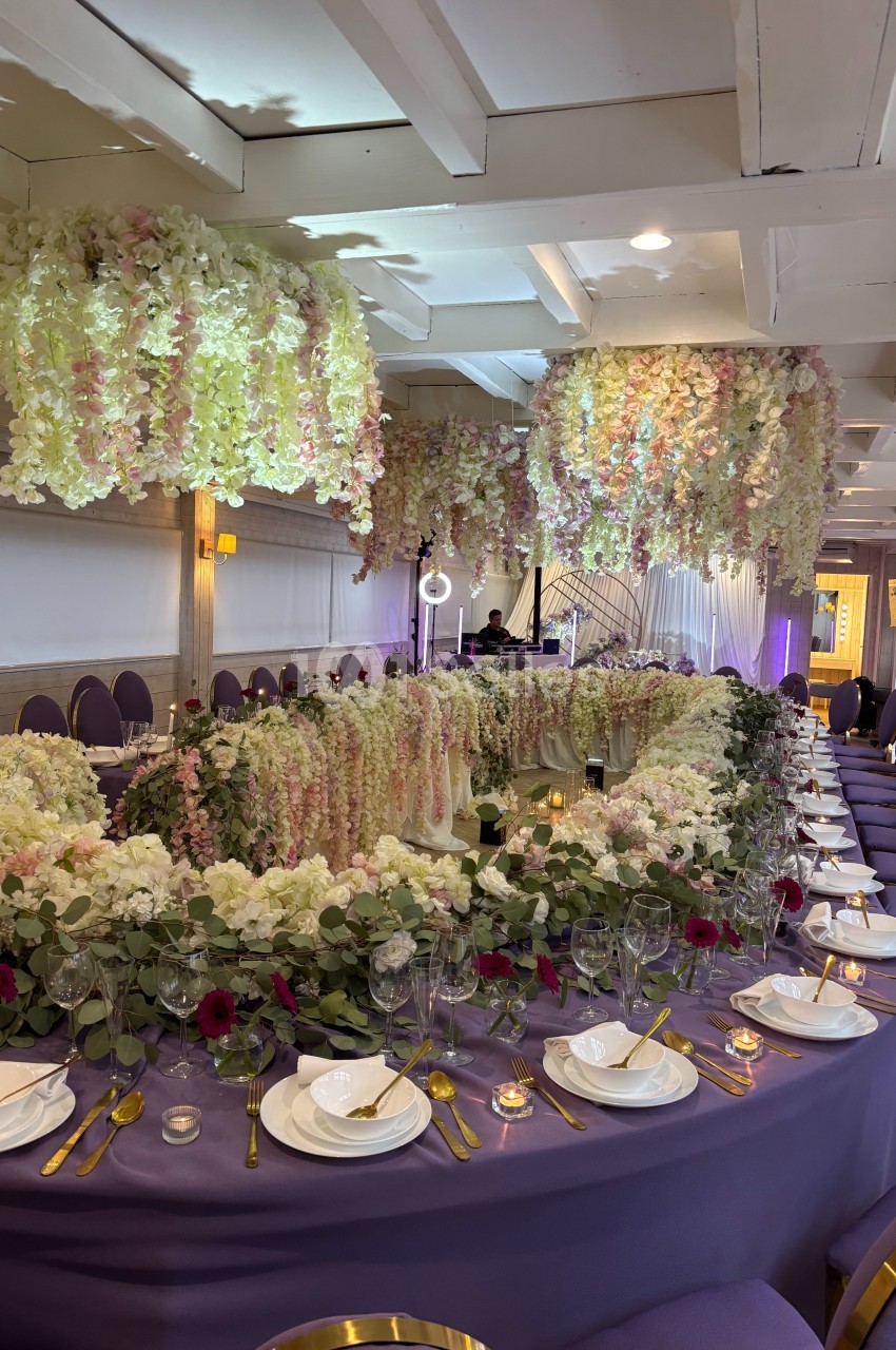 Salle de réception décorée avec des tables violettes, des fleurs suspendues et des arrangements floraux élégants.