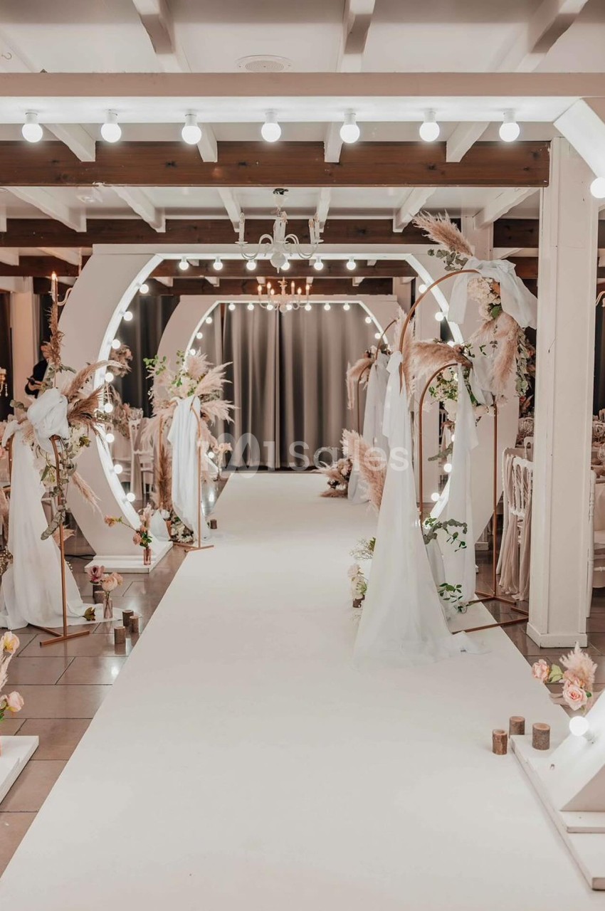 Allée décorée pour un mariage avec arches lumineuses, voilages blancs et arrangements floraux élégants.