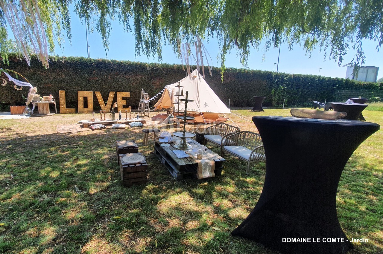 Espace extérieur aménagé avec des meubles en bois, un tipi, et des décorations pour un événement en plein air.