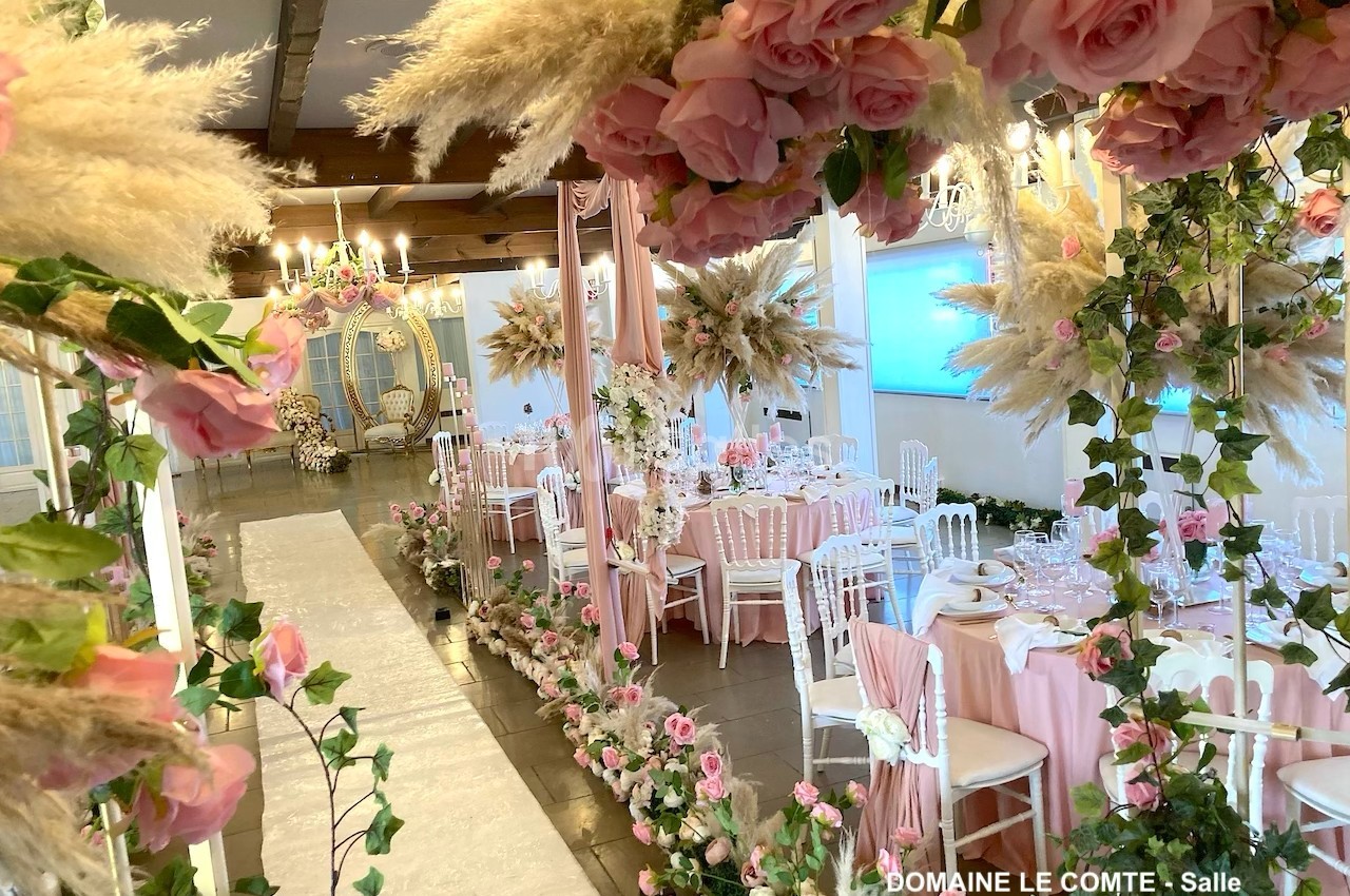 Salle de réception décorée avec des roses roses, des pampas et des tables élégantes pour un événement festif.