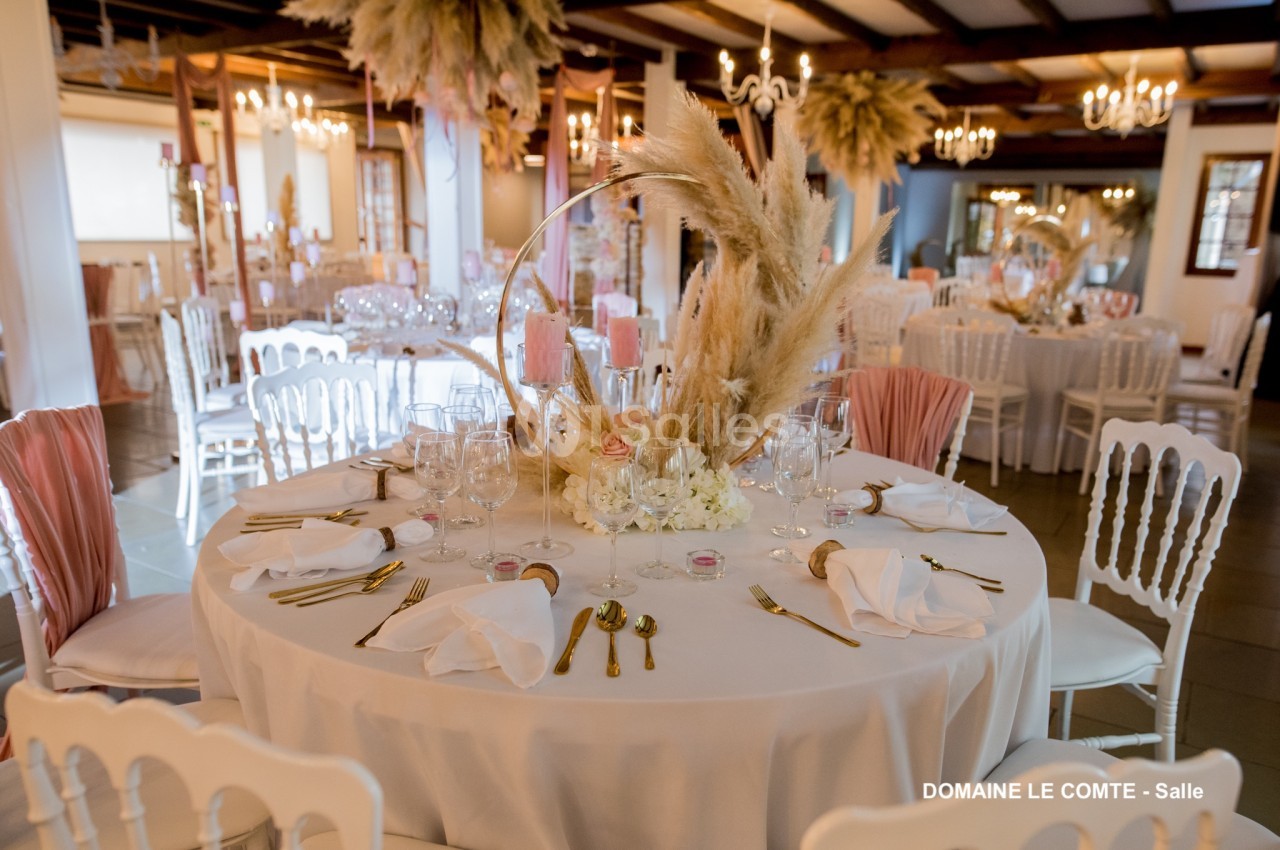 Table ronde élégamment dressée avec des couverts dorés, des serviettes blanches et une décoration florale centrale.
