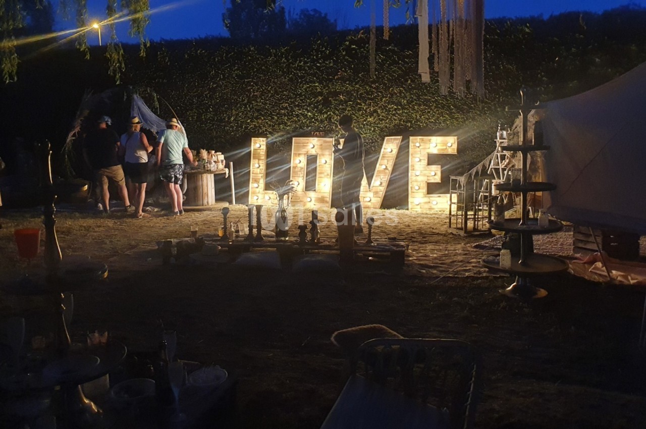 Décoration lumineuse formant le mot ’LOVE’ dans un espace extérieur en soirée, avec des stands et des personnes autour.