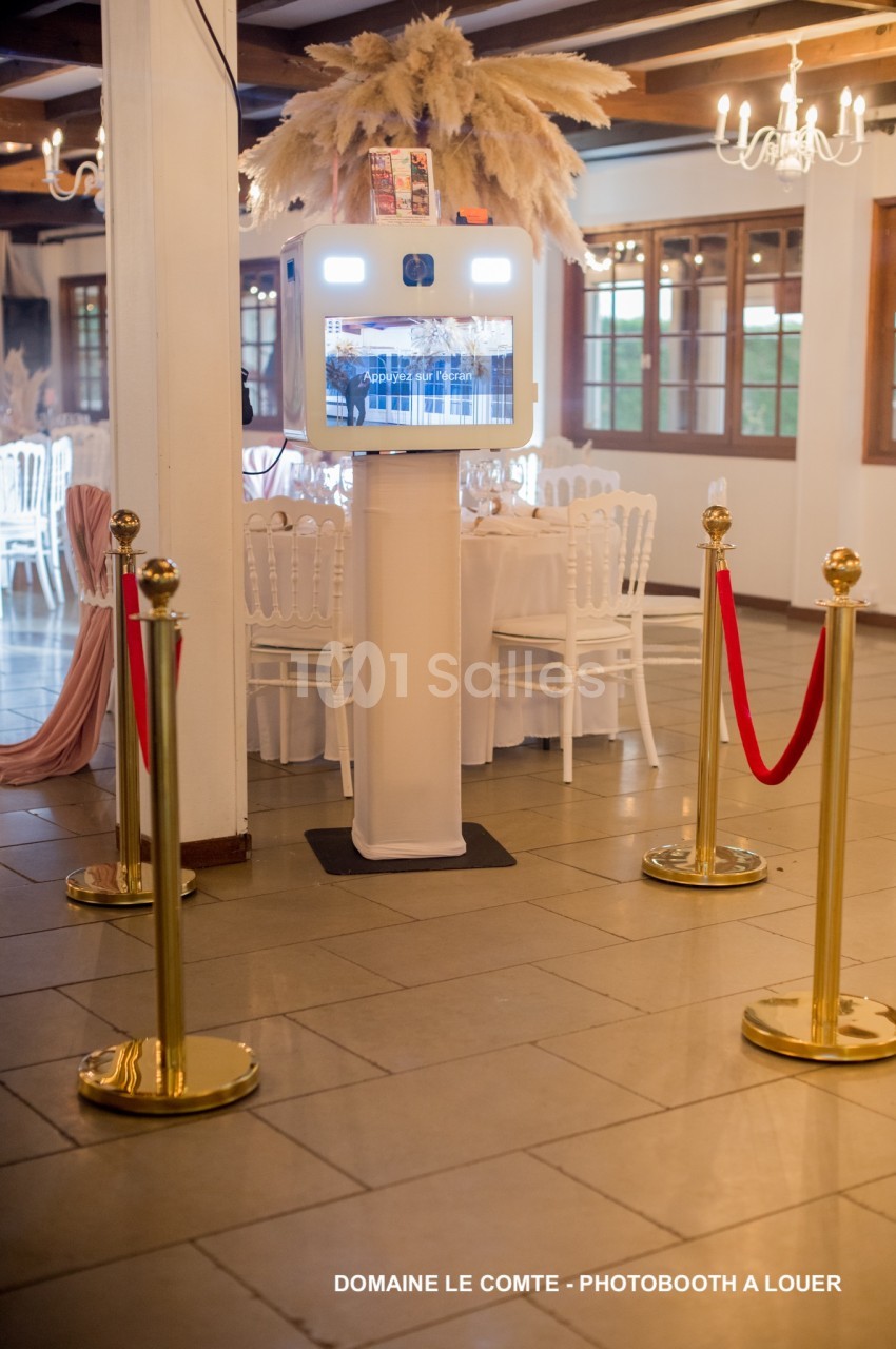 Borne photo interactive installée dans une salle de réception élégante avec chaises blanches et décorations raffinées.