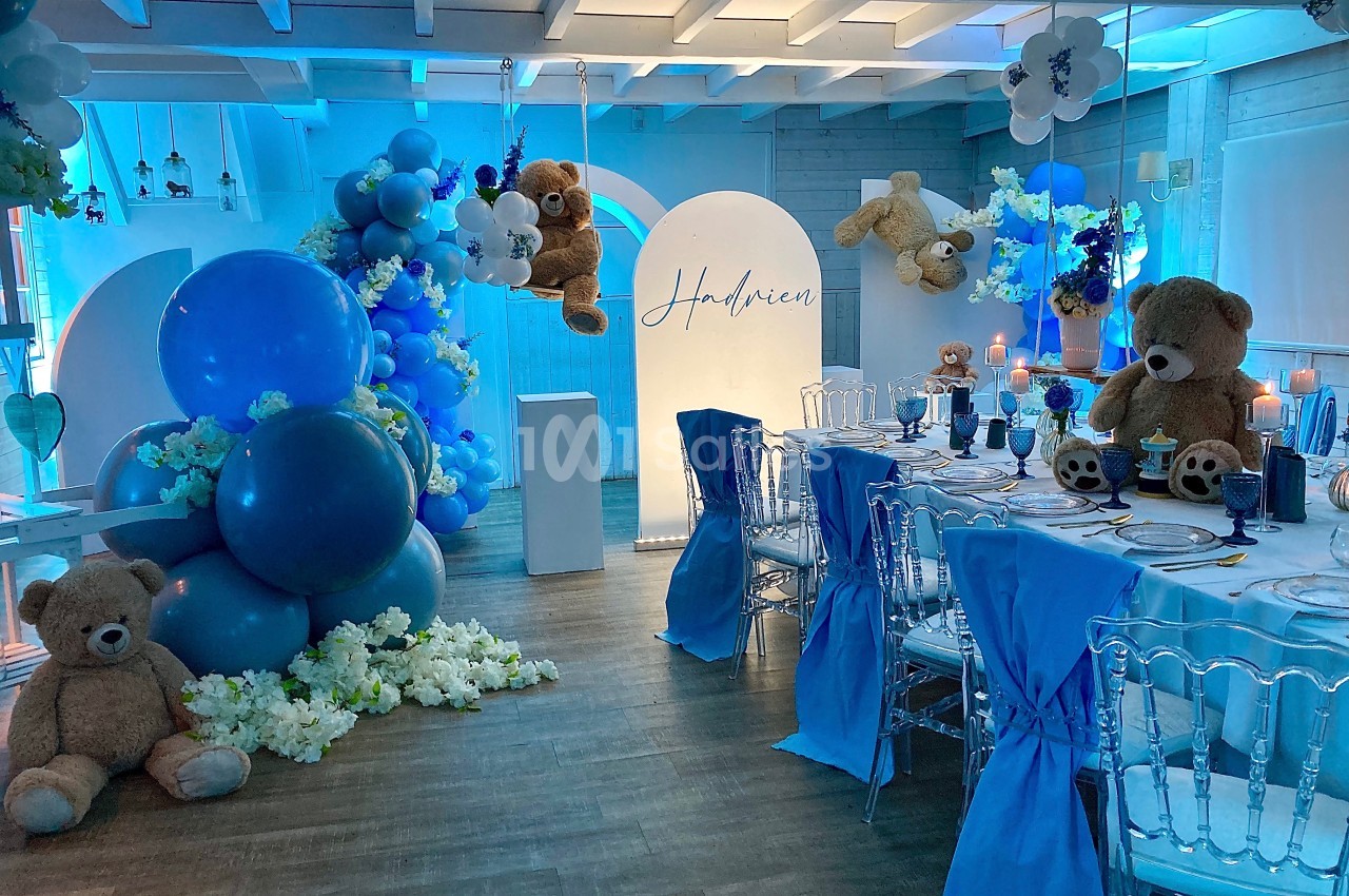 Décoration de salle avec ballons bleus, peluches d'ours et table dressée pour un événement festif.