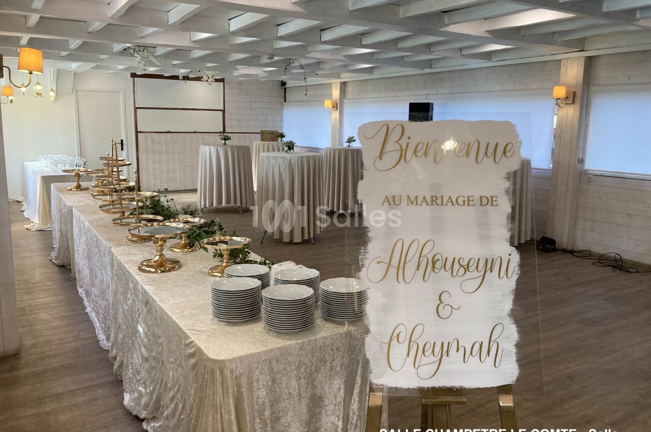 Salle de réception décorée pour un mariage avec une table de buffet garnie et un panneau de bienvenue personnalisé.