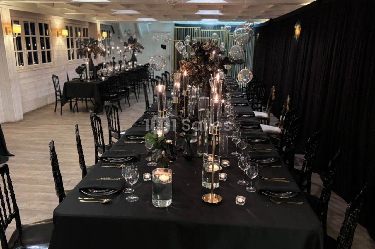 Salle de réception élégante avec longues tables noires décorées de bougies, verrerie et arrangements floraux sombres.