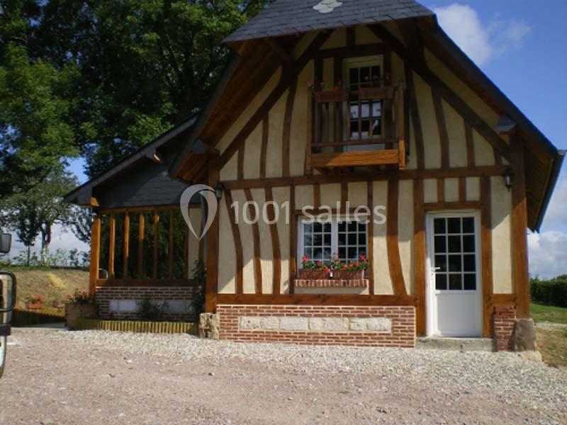 Maison à colombages avec balcon en bois, fenêtres fleuries et toit en ardoise, entourée de verdure.