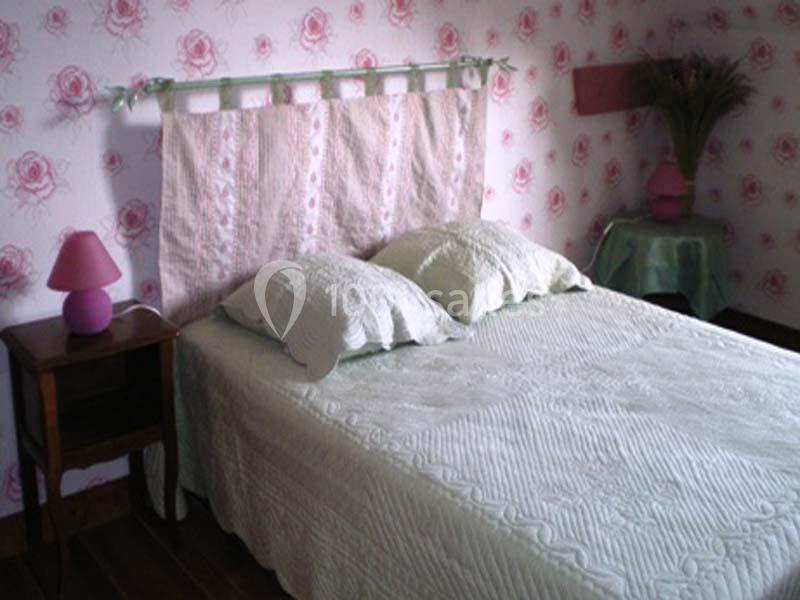 Lit double avec couvre-lit blanc, deux oreillers, table de chevet avec lampe rose et décoration florale sur les murs.