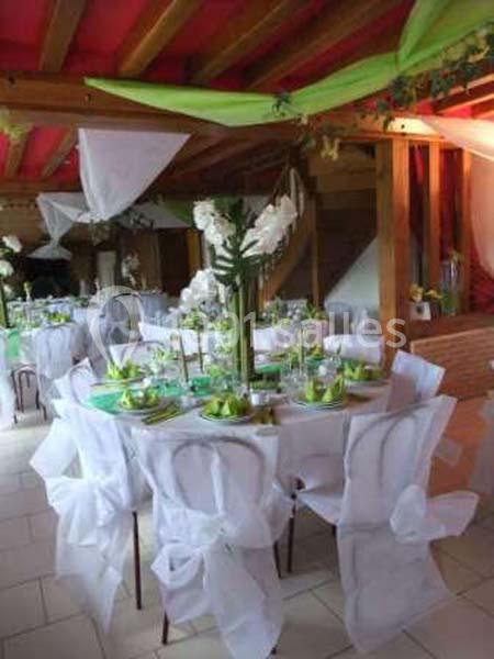 Salle décorée pour un événement avec tables rondes, nappes blanches, chaises ornées de nœuds et centre de table floral.