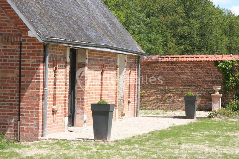 Bâtiment en briques rouges avec toit en ardoise, entouré d'une cour pavée et de jardinières modernes.