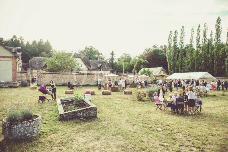 Groupe de personnes réunies dans un jardin avec tables, bottes de foin et tentes en arrière-plan.