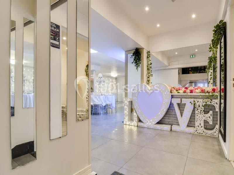Salle de réception décorée avec des lettres lumineuses formant ’LOVE’, des fleurs et des guirlandes végétales.