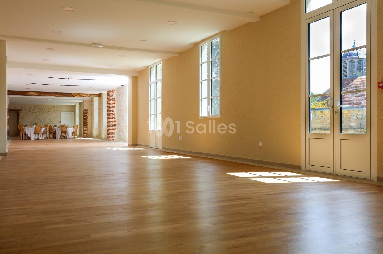 Salle lumineuse avec parquet en bois clair, grandes fenêtres et vue sur un clocher à l'extérieur.