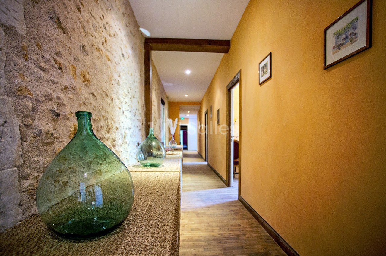 Couloir avec murs en pierre et peinture orange, décoré de bouteilles en verre vert sur une console en bois.
