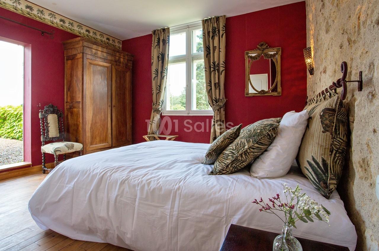 Chambre avec murs rouges, lit double, armoire en bois, fenêtre lumineuse et décoration rustique.