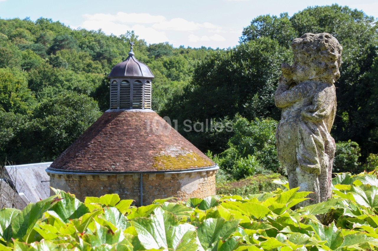 Statue en pierre d'un enfant devant un bâtiment rond avec un toit en tuiles et une coupole, entourés de verdure.