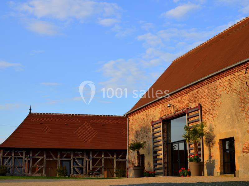 Deux bâtiments en briques et bois avec toits en tuiles, sous un ciel bleu partiellement nuageux.