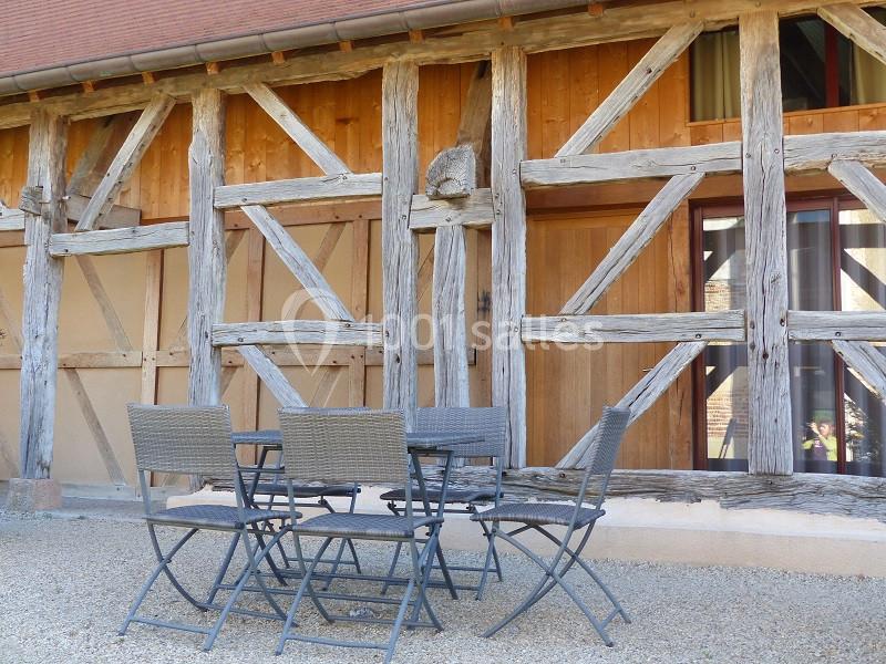 Façade en bois et colombages avec une table et des chaises en métal sur un sol en gravier.
