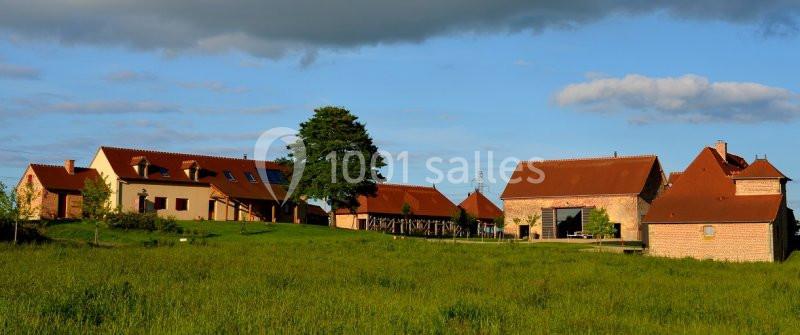 Bâtiments en pierre et toits rouges dans un paysage rural avec pelouse verte et ciel partiellement nuageux.