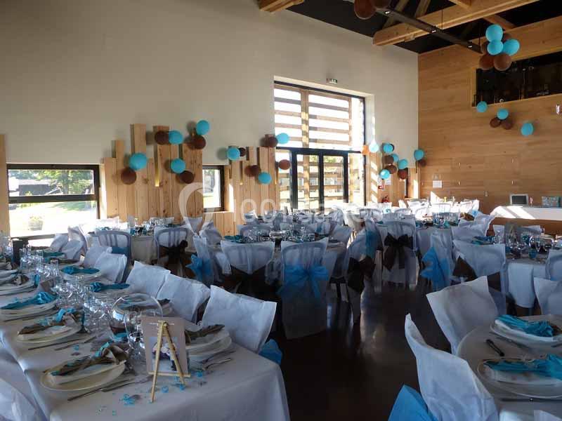 Salle de réception décorée avec des ballons bleus et marron, tables dressées avec nappes blanches et serviettes assorties.