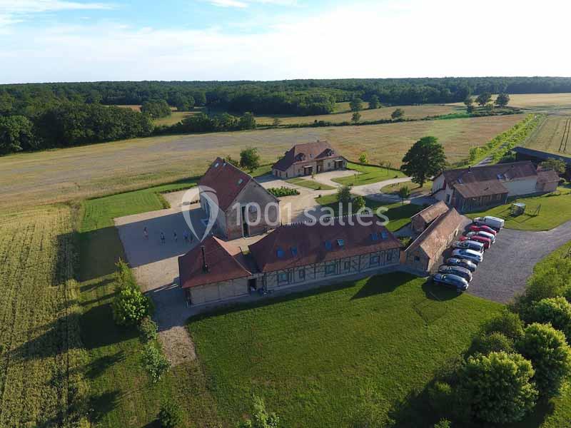 Vue aérienne d'un domaine rural avec bâtiments en pierre, cour centrale, voitures stationnées et champs environnants.
