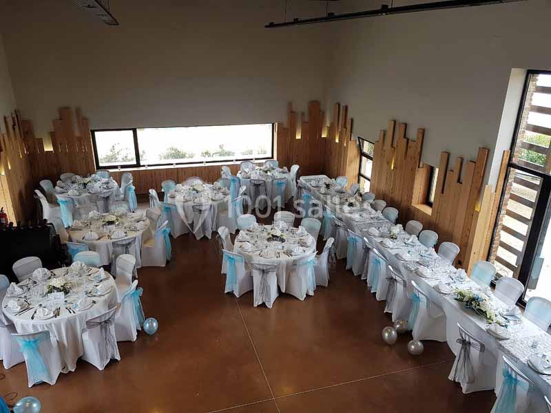 Salle de réception décorée avec des tables rondes, nappes blanches et rubans bleus, prête pour un événement.