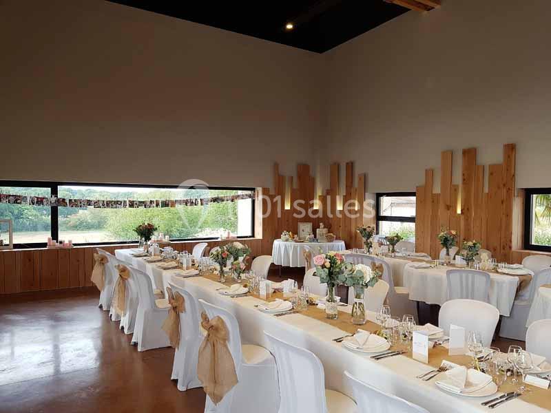 Salle de réception décorée pour un mariage, avec tables dressées, nappes blanches et compositions florales.