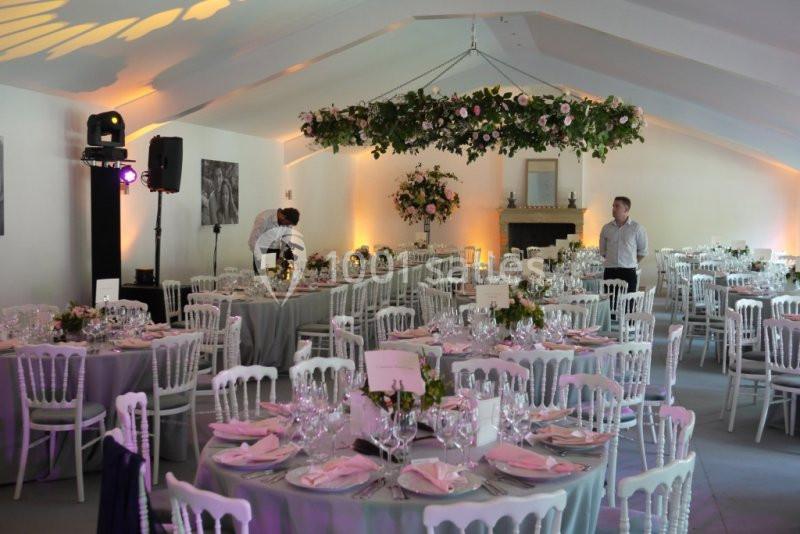 Salle de réception décorée pour un mariage, avec tables dressées, nappes grises, fleurs et éclairage chaleureux.