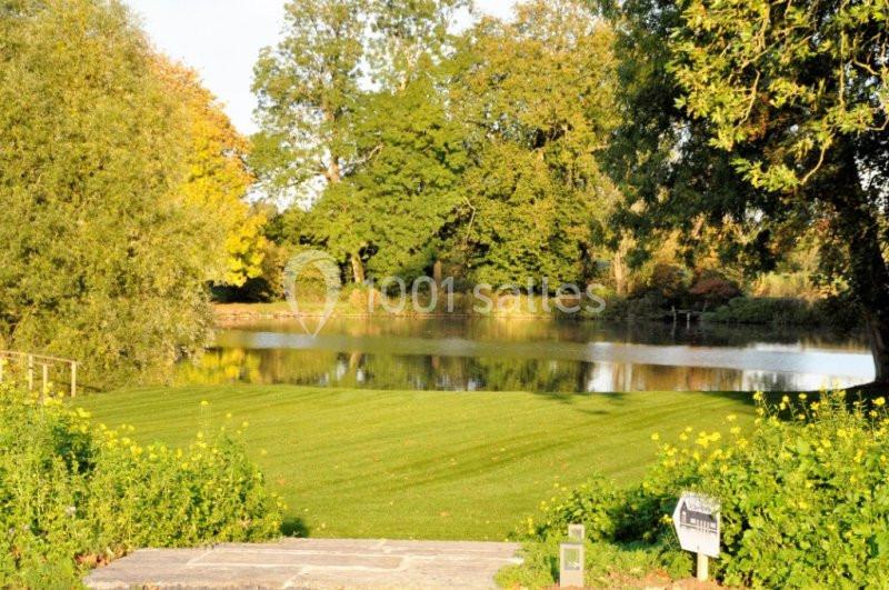 Vue d'un jardin verdoyant avec une pelouse bien entretenue, bordé d'arbres et d'un étang paisible en arrière-plan.