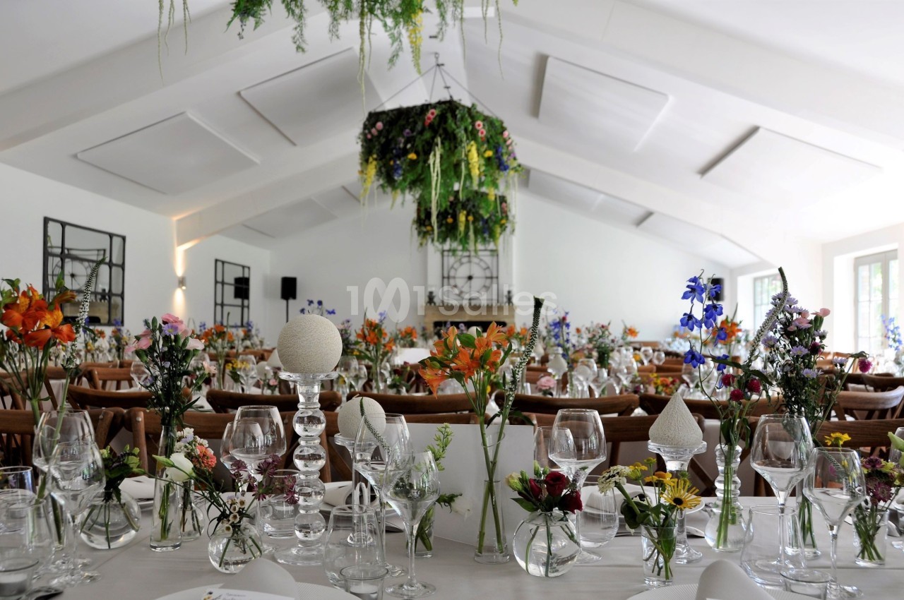 Salle de réception lumineuse décorée de fleurs colorées sur des tables dressées avec vaisselle élégante.