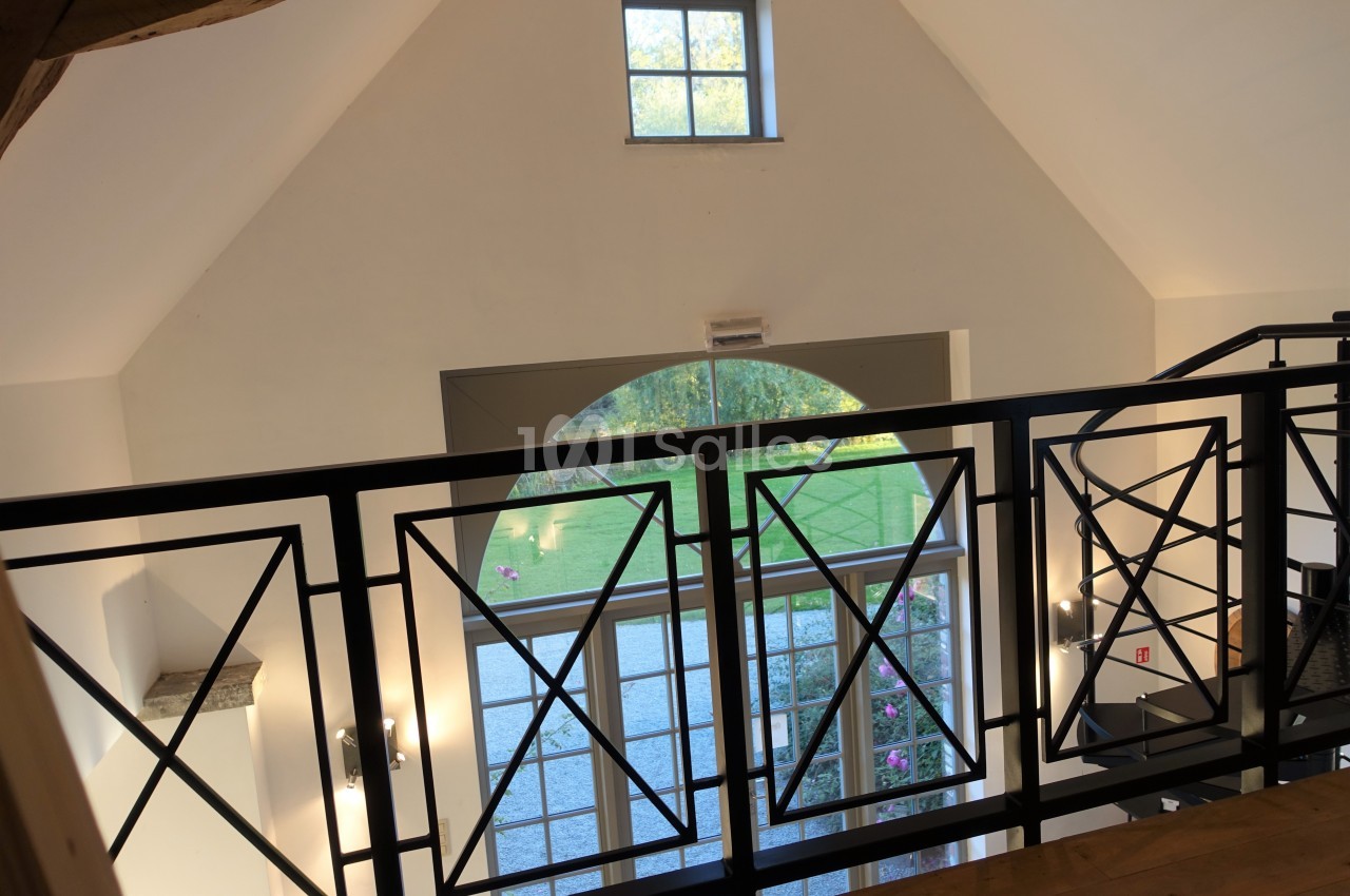 Vue intérieure d'une mezzanine avec garde-corps en métal, donnant sur une grande baie vitrée et un jardin extérieur.