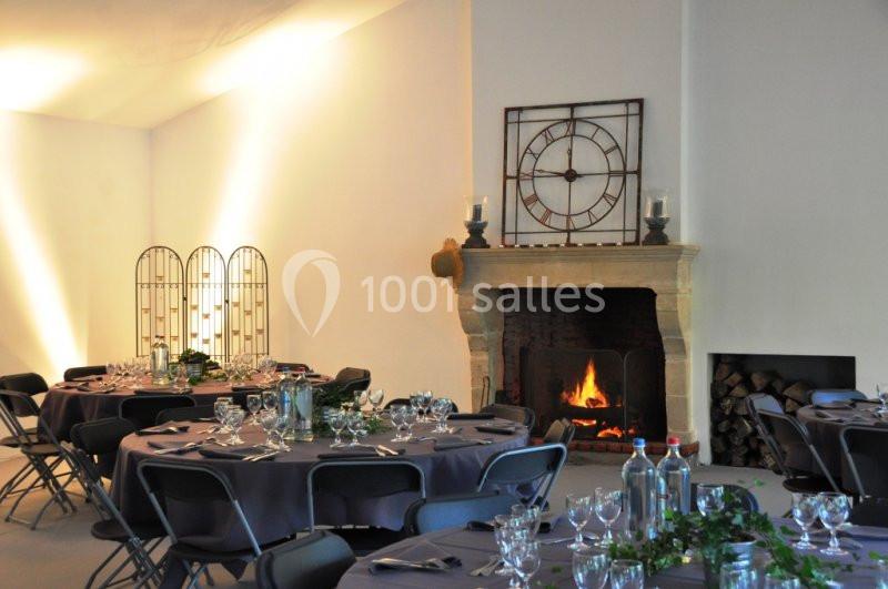 Salle de réception décorée avec des tables rondes dressées, une cheminée allumée et une grande horloge murale.