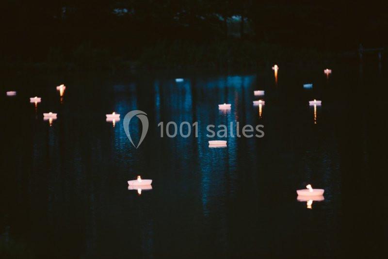 Des bougies flottent sur un lac sombre, reflétant leur lumière dans l'eau calme sous un ciel nocturne.