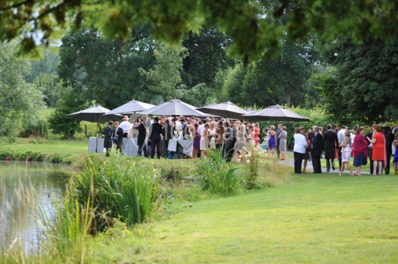 Groupe de personnes rassemblées près d'un étang, autour de tables et parasols dans un cadre verdoyant.