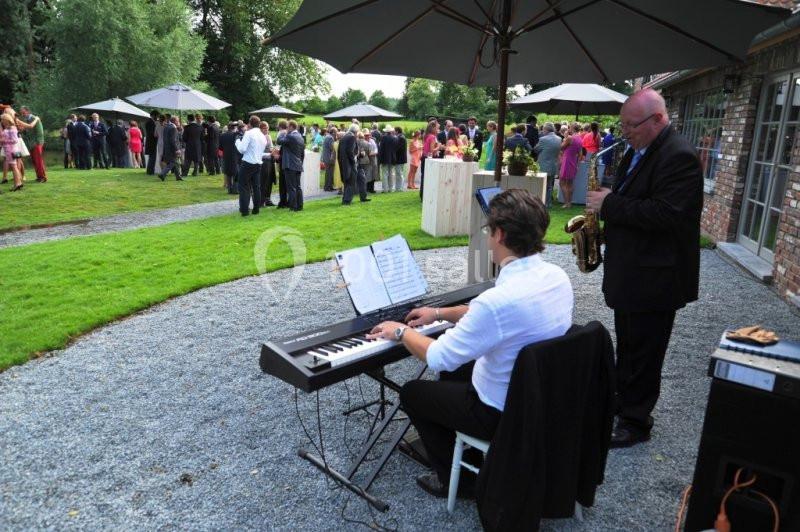 Un pianiste et un saxophoniste jouent en extérieur lors d'un événement avec des invités rassemblés sur une pelouse.