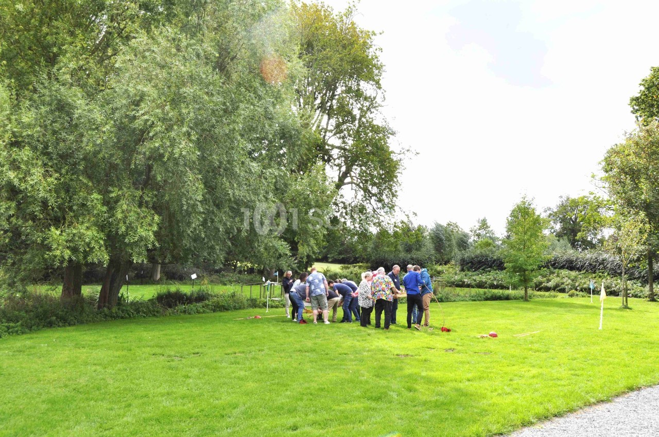 Un groupe de personnes rassemblées sur une pelouse verte dans un parc, entouré d'arbres et de végétation.