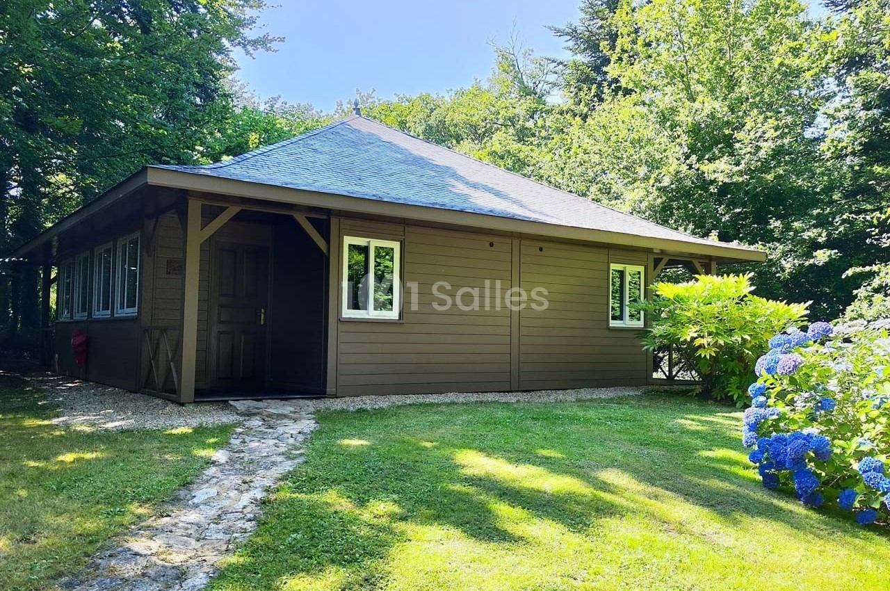 Chalet en bois avec toit en ardoise, entouré de verdure et hortensias, éclairé par une lumière estivale.