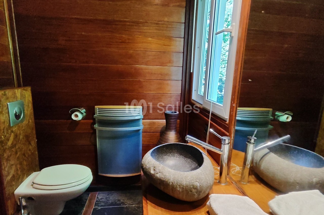 Salle de bain avec murs en bois, lavabo en pierre, toilettes, miroir, fenêtre et accessoires modernes.