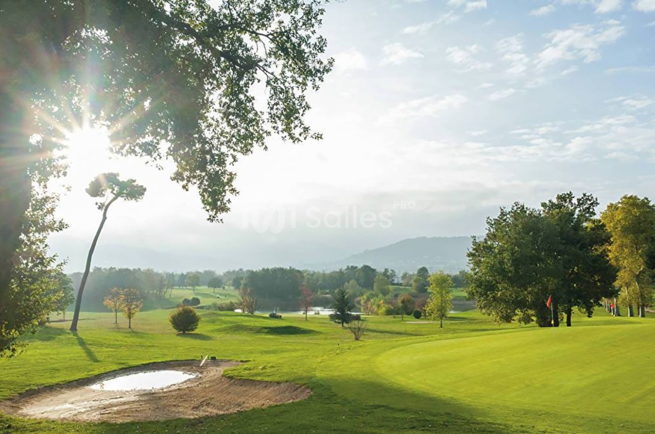 Paysage de golf avec un terrain verdoyant, des arbres, un bunker de sable et un soleil éclatant à l'horizon.
