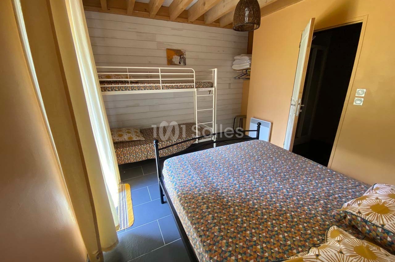 Chambre avec un lit double, des lits superposés, murs en bois clair et plafond avec poutres apparentes.