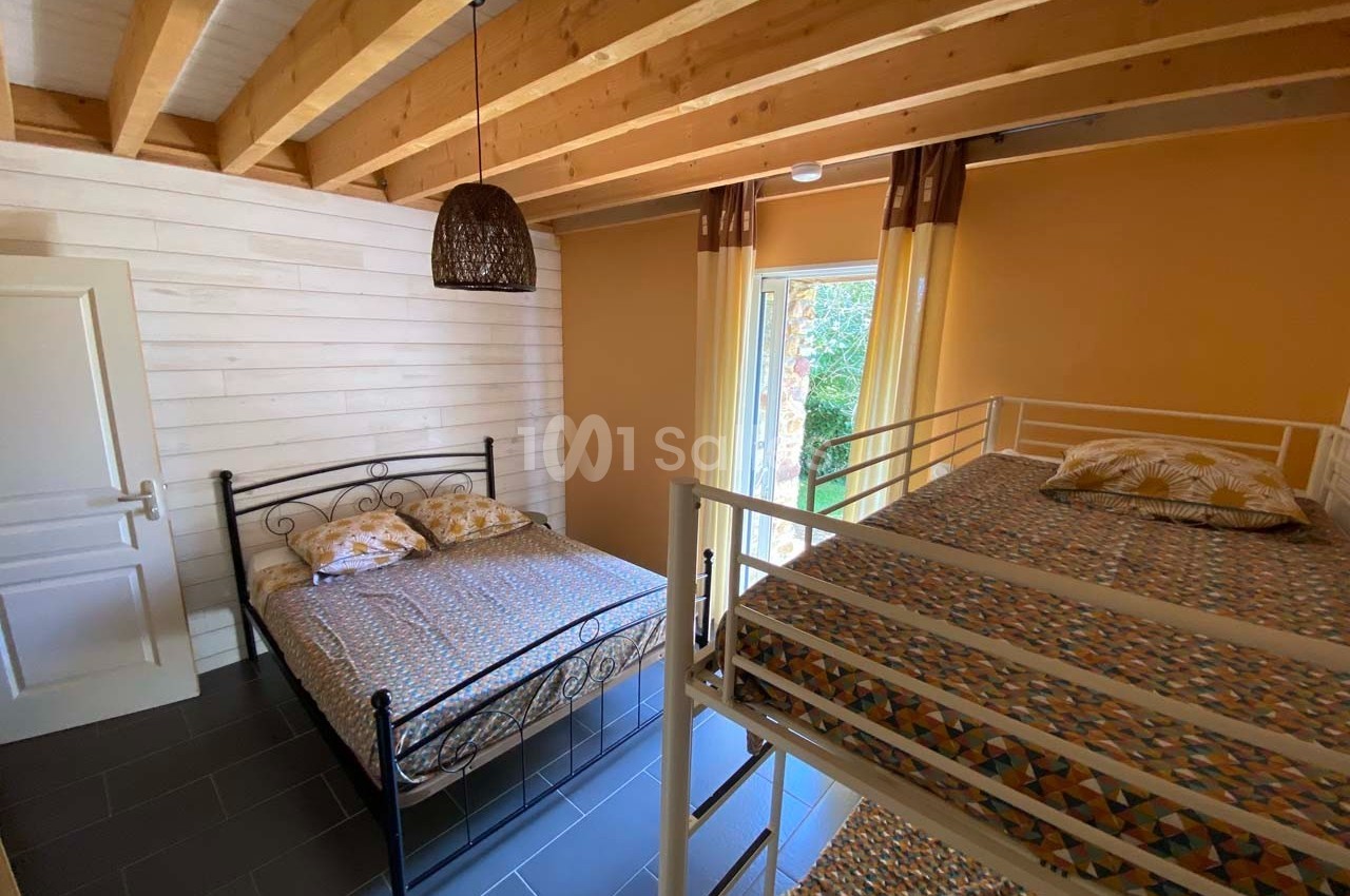 Chambre avec un lit double, des lits superposés, murs en bois clair, plafond avec poutres apparentes et fenêtre donnant sur…