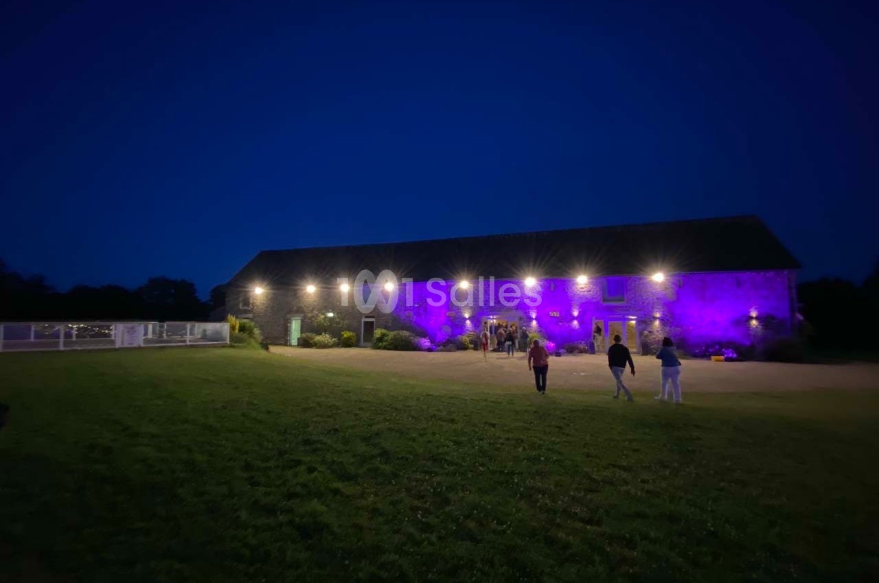 Bâtiment en pierre éclairé par des lumières violettes et blanches, avec quelques personnes marchant sur une pelouse au…
