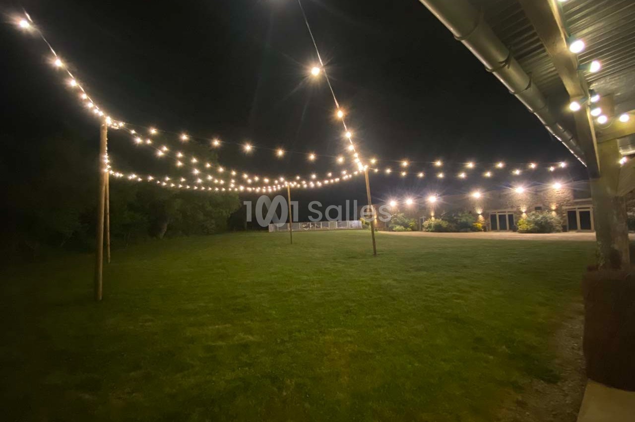 Guirlandes lumineuses suspendues au-dessus d'une pelouse éclairée, près d'un bâtiment en soirée.