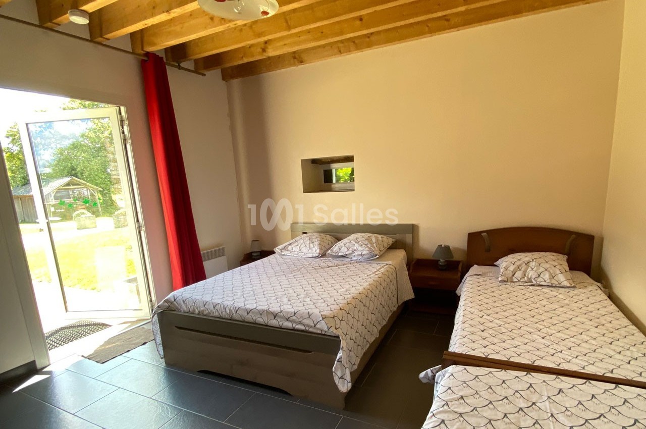 Chambre lumineuse avec un lit double, un lit simple, des poutres apparentes et une porte ouverte sur un jardin.